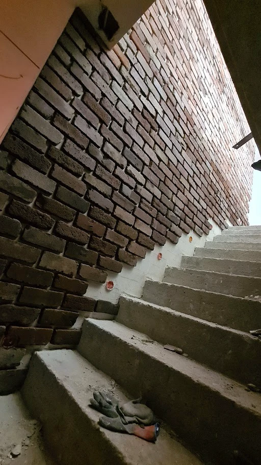Betonowe schody przy odsłoniętej ceglanej ścianie w trakcie remontu kościoła z rękawicami na stopniach