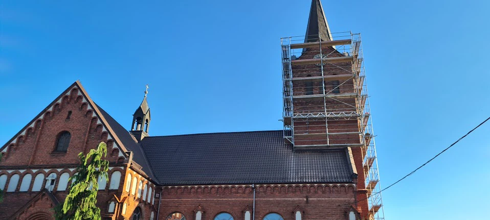 Zabytkowy czerwony kościół z rusztowaniem na wieży podczas remontu kościoła