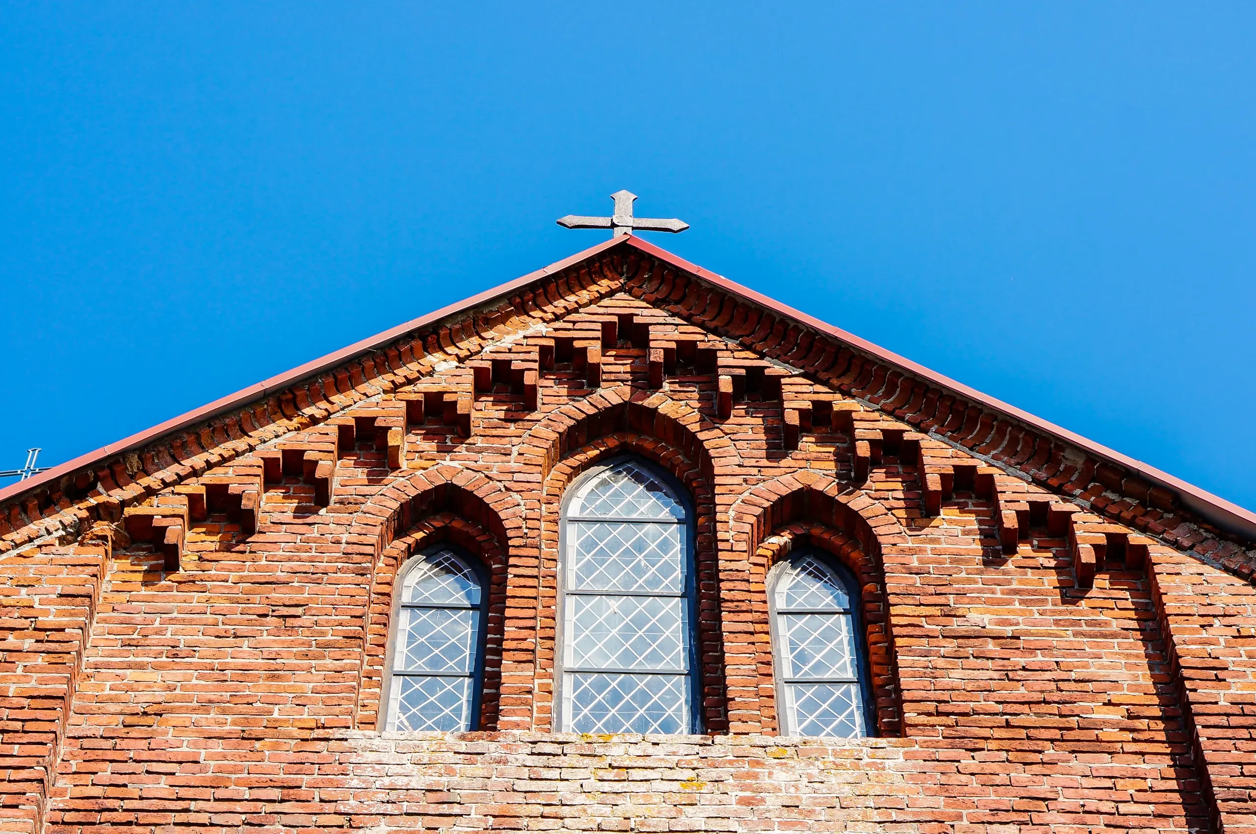 Fragment ceglastej elewacji kościoła z trójką ostrołukowych okien i krzyżem – Renowacja kościołów