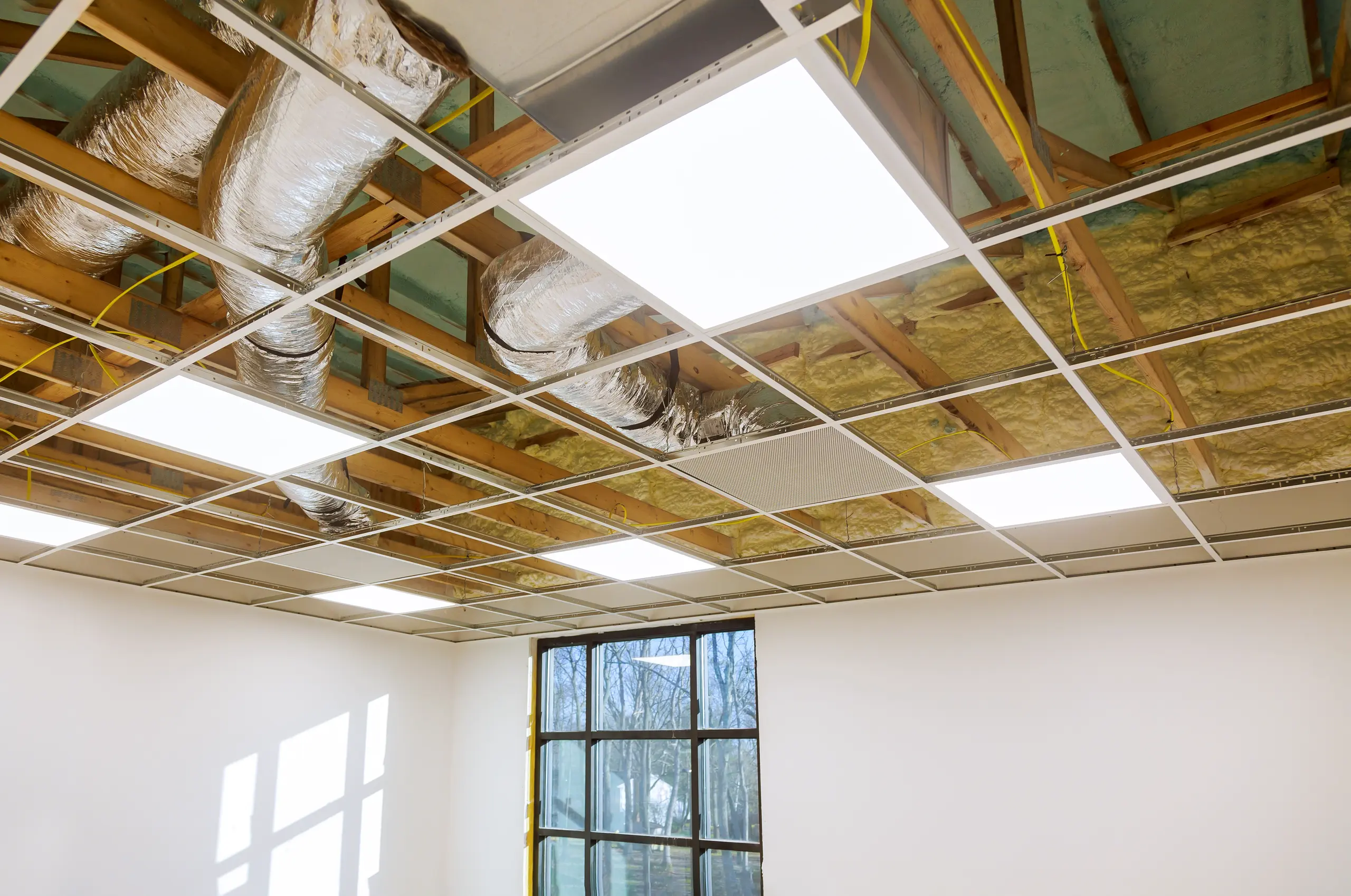 Montaż sufitu podwieszanego z panelami LED i widoczną izolacją oraz instalacją przewodów