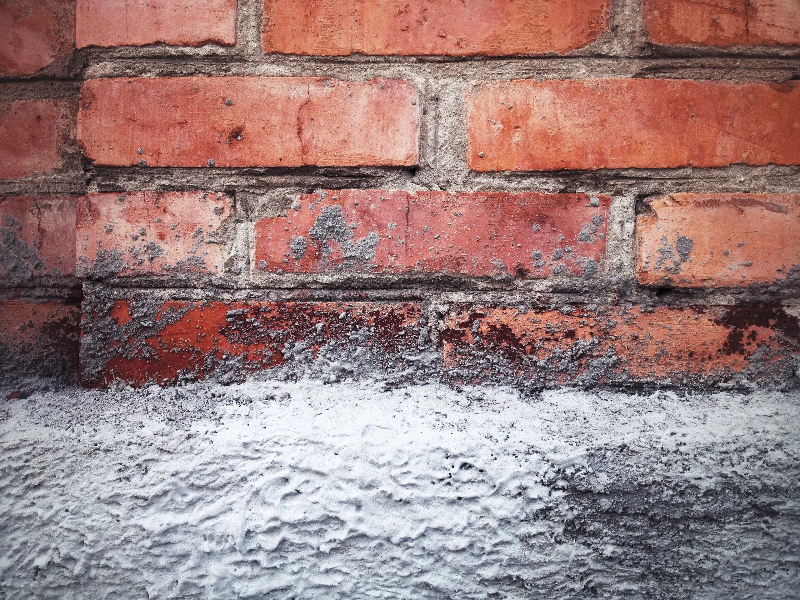 Fragment muru z widoczną czerwoną cegłą i częściowo nałożonym białym gipsem – gipsowanie ścian