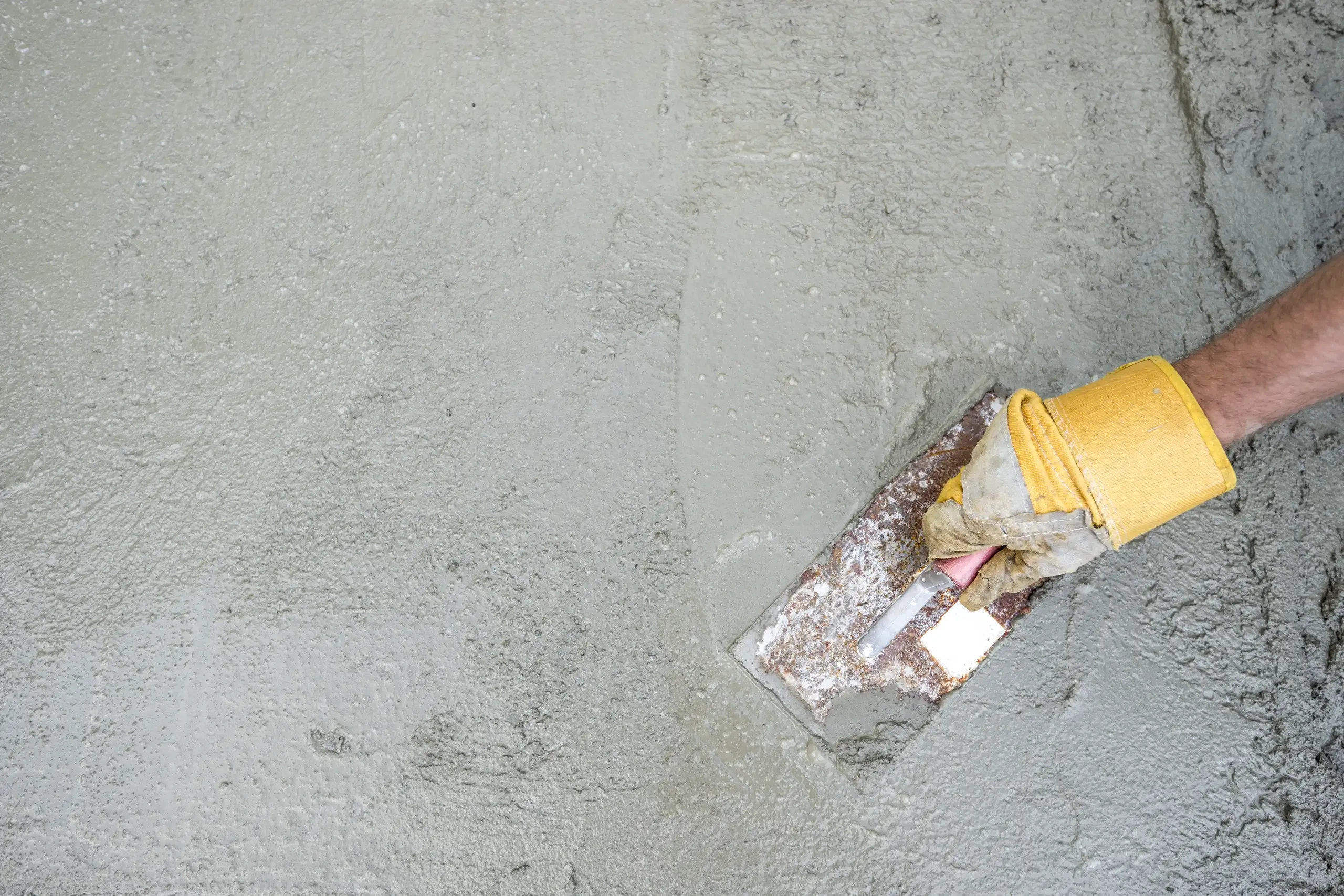 Ręka w rękawicy wygładza świeżą wylewkę betonową pacą – Posadzki